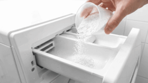 Waschpulver wird in das Fach der Waschmaschine gef&uuml;llt, um Bettw&auml;sche hygienisch zu waschen.