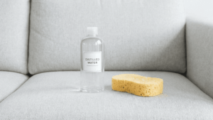 Flasche mit destilliertem Wasser und Schwamm auf einem Sofa gegen Wasserr&auml;nder.