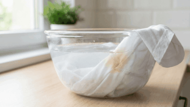 Weißes Kleidungsstück mit eingetrocknetem Schweißfleck eingeweicht in einer Glasschüssel mit Wasser – Methode zum Lösen alter Schweißflecken