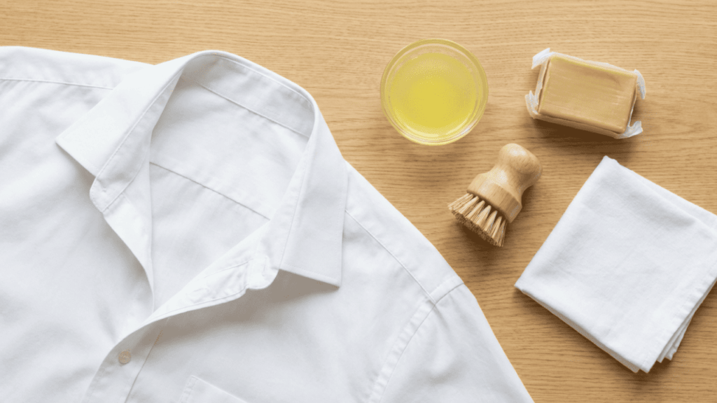 Wei&szlig;es Business-Hemd neben Gallseife, Zitronensaft, B&uuml;rste und Tuch auf einem Holztisch &ndash; Hausmittel zur Schwei&szlig;fleckenentfernung aus Hemden