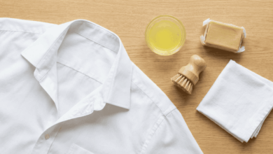 Weißes Business-Hemd neben Gallseife, Zitronensaft, Bürste und Tuch auf einem Holztisch – Hausmittel zur Schweißfleckenentfernung aus Hemden